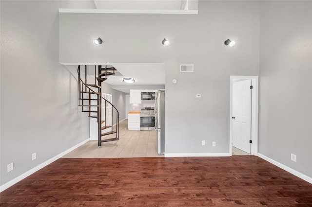 12900 Walden Rd Unit 406D, Montgomery, TX 77356 - unfurnished living room with baseboards, light wood finished floors, stairs, and a towering ceiling