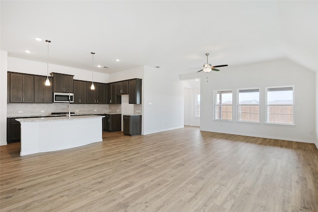 27519 Beachside Arbor Dr, Katy, TX 77493 - kitchen with stainless steel microwave, open floor plan, backsplash, light countertops, and dark brown cabinetry