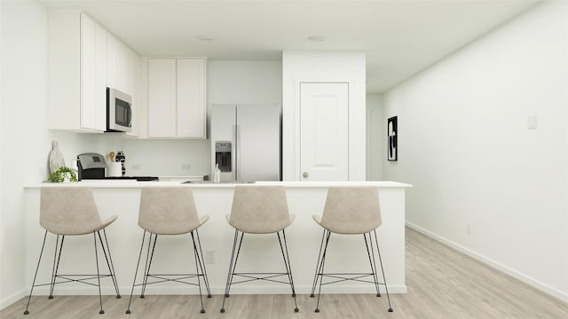 10823 Red Orchid Dr, Houston, TX 77016 - kitchen featuring fridge with ice dispenser, a breakfast bar, light wood finished floors, stainless steel microwave, and white cabinets