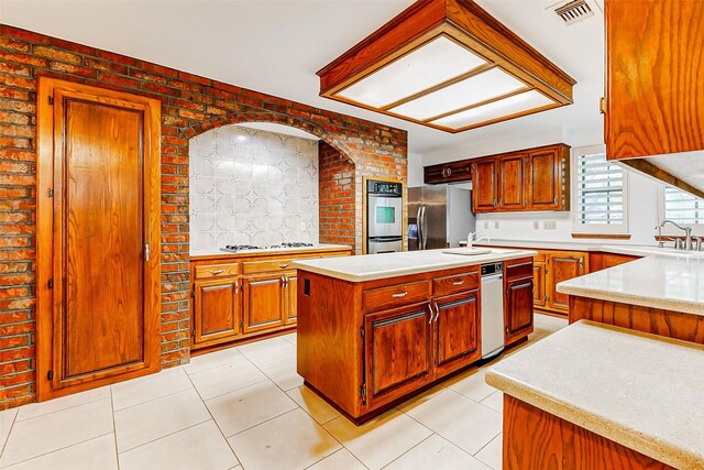 6225 Morton Rd, Katy, TX 77493 - kitchen featuring stainless steel appliances, light countertops, a center island with sink, light tile patterned flooring, and brick wall
