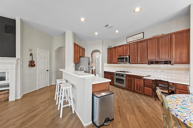 6219 Royal Hollow Ln, Katy, TX 77450 - kitchen featuring stainless steel appliances, arched walkways, a kitchen breakfast bar, tasteful backsplash, and light wood finished floors