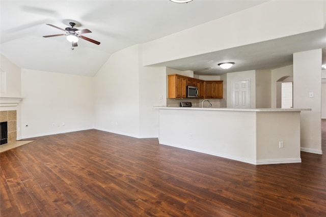 19511 Ingham Dr, Katy, TX 77449 - unfurnished living room with vaulted ceiling, ceiling fan, dark wood-style flooring, a tiled fireplace, and arched walkways