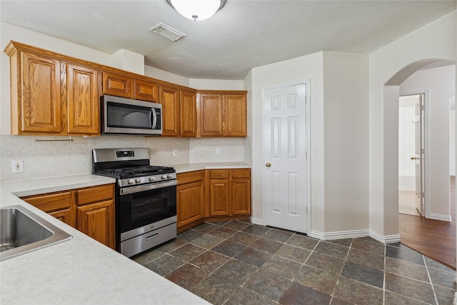 19511 Ingham Dr, Katy, TX 77449 - kitchen featuring stainless steel appliances, arched walkways, light countertops, and brown cabinets