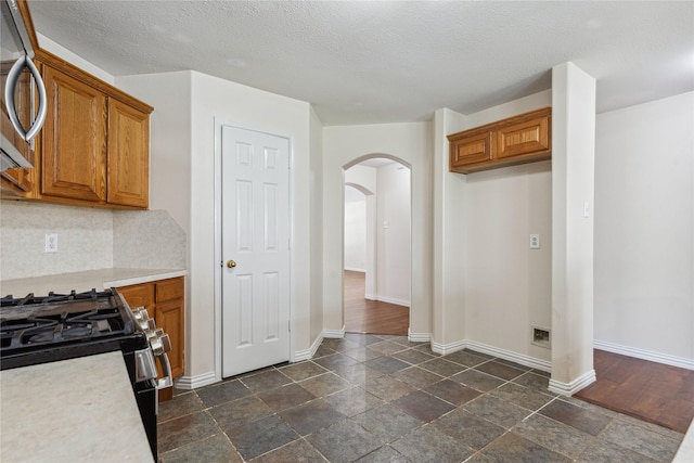 19511 Ingham Dr, Katy, TX 77449 - kitchen featuring stainless steel range with gas stovetop, arched walkways, brown cabinets, light countertops, and dark stone finish floors