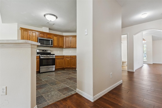 19511 Ingham Dr, Katy, TX 77449 - kitchen with appliances with stainless steel finishes, arched walkways, light countertops, brown cabinets, and dark wood finished floors