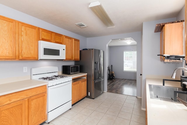 24027 Pinecreek Pt, Spring, TX 77373 - kitchen featuring appliances with stainless steel finishes, light countertops, arched walkways, light tile patterned floors, and a sink