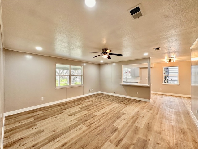 7845 Bonaire St, Houston, TX 77028 - unfurnished living room with light wood-style floors, a ceiling fan, healthy amount of natural light, baseboards, and a textured ceiling