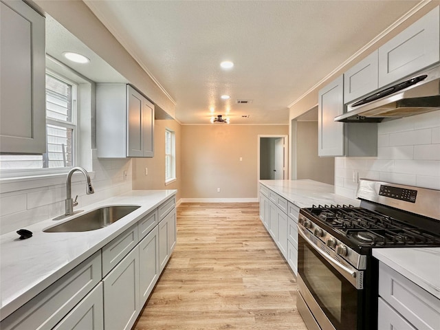 7845 Bonaire St, Houston, TX 77028 - kitchen featuring stainless steel gas range, a sink, under cabinet range hood, light wood-style floors, and baseboards
