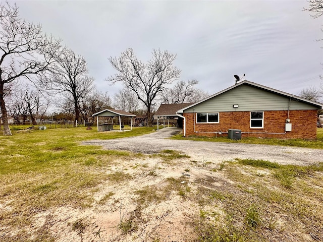 7845 Bonaire St, Houston, TX 77028 - view of side of property with gravel driveway, brick siding, a carport, a yard, and central AC