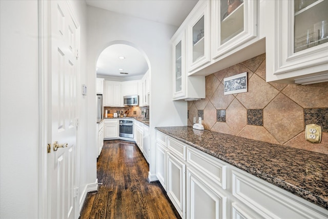 1202 Marconi St, Houston, TX 77019 - kitchen with stainless steel appliances, backsplash, dark stone countertops, arched walkways, and white cabinetry