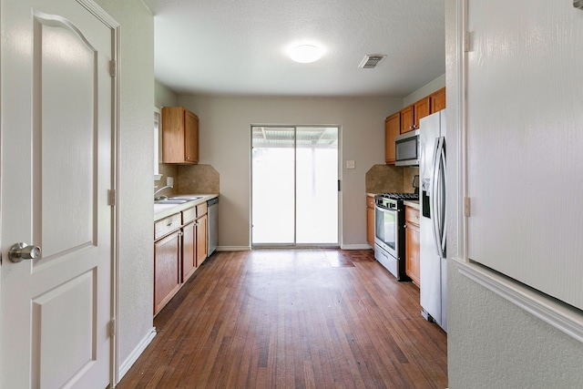 12518 Rosslare Dr, Houston, TX 77066 - kitchen featuring appliances with stainless steel finishes, backsplash, dark wood finished floors, and brown cabinetry