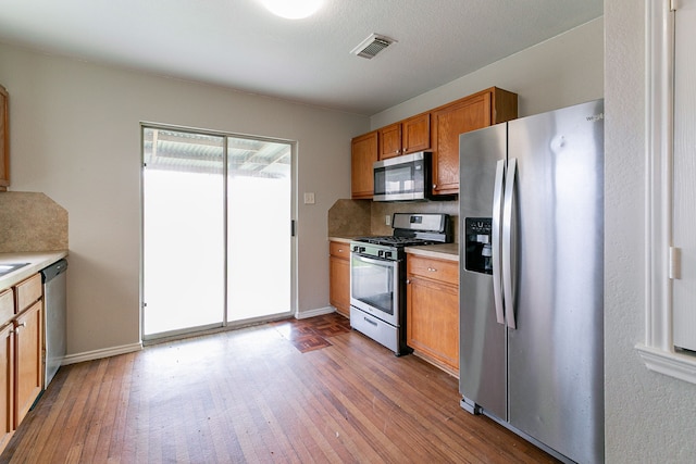 12518 Rosslare Dr, Houston, TX 77066 - kitchen featuring stainless steel appliances, hardwood / wood-style floors, brown cabinets, light countertops, and backsplash