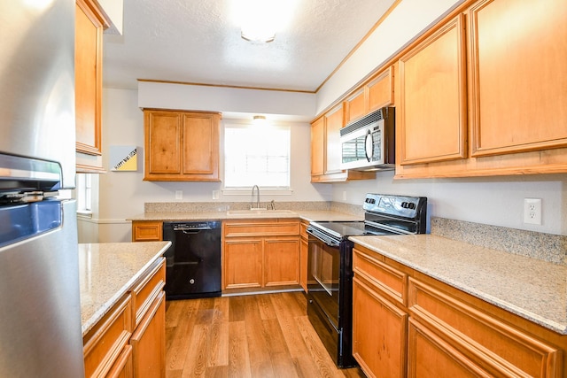 25635 Glen Loch Dr, Spring, TX 77380 - kitchen featuring black appliances, a sink, light wood-style flooring, light stone counters, and brown cabinetry
