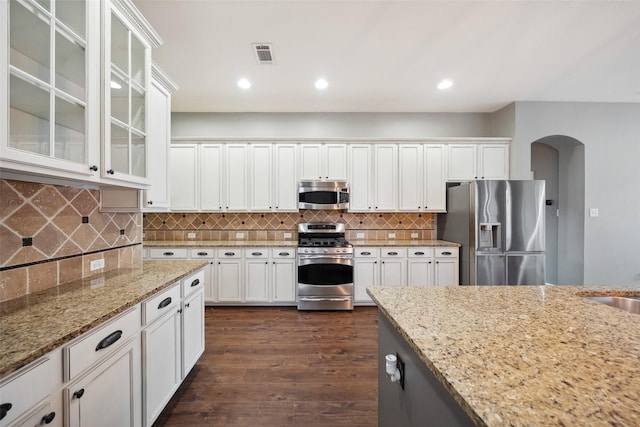 2935 Red Maple Dr, Katy, TX 77494 - kitchen with appliances with stainless steel finishes, arched walkways, light stone countertops, white cabinetry, and dark wood-type flooring