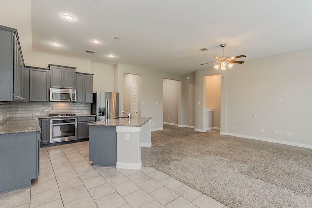 13605 Northline Lake Dr, Houston, TX 77044 - kitchen featuring stainless steel appliances, a ceiling fan, decorative backsplash, light stone countertops, and a center island with sink