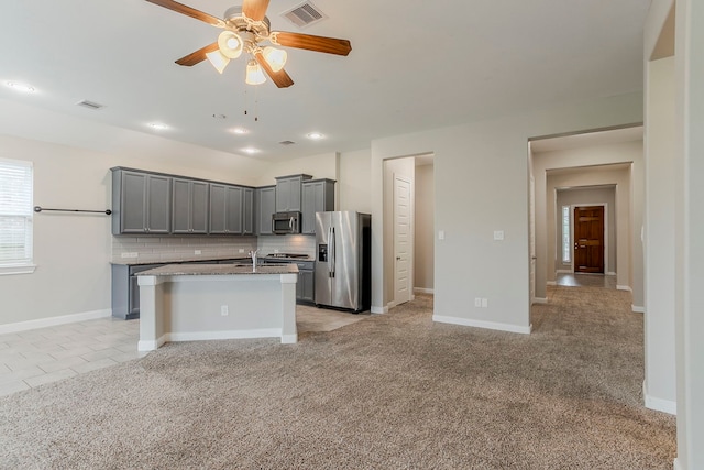 13605 Northline Lake Dr, Houston, TX 77044 - kitchen featuring appliances with stainless steel finishes, gray cabinets, a ceiling fan, a center island with sink, and tasteful backsplash