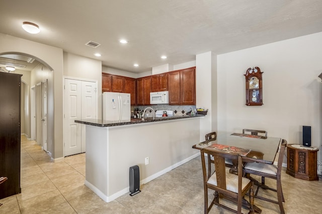 18720 Serenity Loch Dr, Spring, TX 77379 - kitchen with white appliances, arched walkways, dark stone countertops, light tile patterned floors, and a peninsula