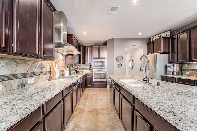 21806 W Firemist Ct, Cypress, TX 77433 - kitchen with a sink, wall chimney exhaust hood, stainless steel appliances, arched walkways, and tasteful backsplash