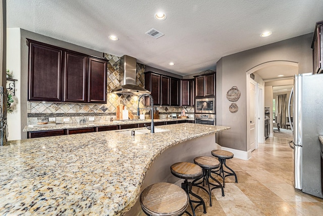 21806 W Firemist Ct, Cypress, TX 77433 - kitchen with wall chimney range hood, appliances with stainless steel finishes, arched walkways, a sink, and tasteful backsplash