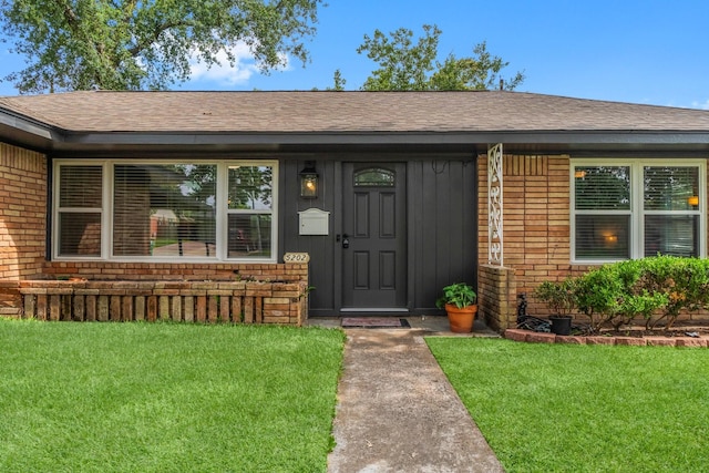 5202 Libbey Ln, Houston, TX 77092 - view of exterior entry with a shingled roof, a yard, and brick siding