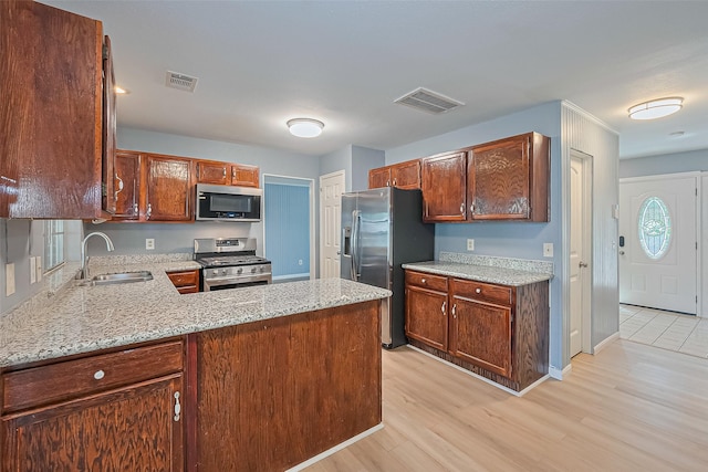 1010 Cheyenne Meadows Dr, Katy, TX 77450 - kitchen with stainless steel appliances, a sink, light wood-style flooring, light stone counters, and a peninsula