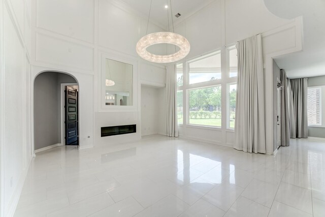 3650 Sage Hollow Dr, Spring, TX 77386 - unfurnished living room featuring a high ceiling, arched walkways, healthy amount of natural light, a glass covered fireplace, and light tile patterned floors