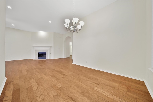 10938 Glenrothers Dr, Richmond, TX 77407 - unfurnished living room featuring arched walkways, a chandelier, recessed lighting, light wood finished floors, and a tiled fireplace