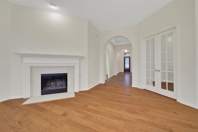 10938 Glenrothers Dr, Richmond, TX 77407 - unfurnished living room with light wood-type flooring, arched walkways, french doors, and a tile fireplace