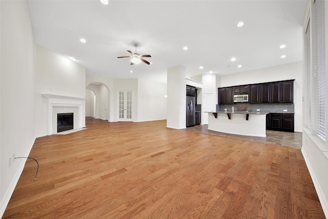 10938 Glenrothers Dr, Richmond, TX 77407 - unfurnished living room with a ceiling fan, light wood-style flooring, recessed lighting, a fireplace with flush hearth, and arched walkways