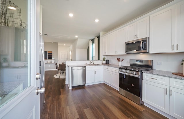 25319 Merino Dr, Magnolia, TX 77355 - kitchen featuring appliances with stainless steel finishes, dark wood-type flooring, white cabinets, light stone countertops, and a peninsula