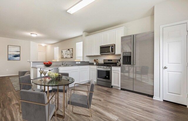 25323 Merino Dr, Magnolia, TX 77355 - kitchen with appliances with stainless steel finishes, wood finished floors, white cabinetry, a peninsula, and baseboards