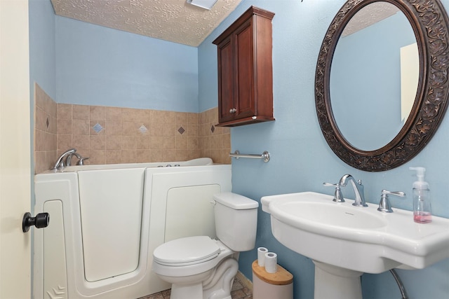 414 Enfield Dr, Highlands, TX 77562 - bathroom featuring a garden tub, a sink, toilet, and a textured ceiling