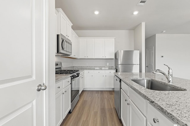 7606 Thrips Ln, Richmond, TX 77469 - kitchen featuring stainless steel appliances, a sink, white cabinets, light wood finished floors, and light stone countertops