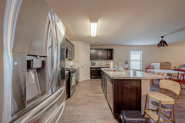 2026 Naplechase Crest Dr, Spring, TX 77373 - kitchen with stainless steel appliances, dark brown cabinetry, a center island with sink, backsplash, and a breakfast bar