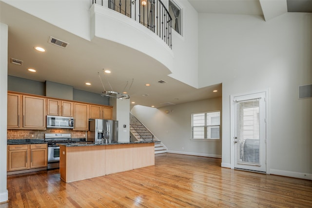 2915 Pease St, Houston, TX 77003 - kitchen featuring appliances with stainless steel finishes, a kitchen island with sink, a towering ceiling, tasteful backsplash, and wood finished floors