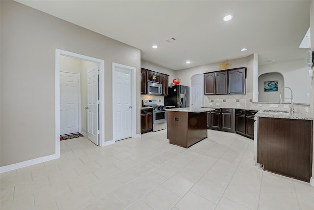 4114 Elk Bluff Ln, Katy, TX 77494 - kitchen featuring appliances with stainless steel finishes, a sink, tasteful backsplash, dark brown cabinets, and a kitchen island