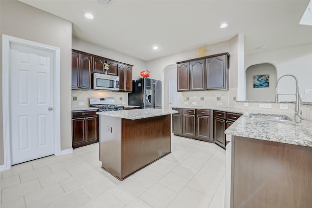 4114 Elk Bluff Ln, Katy, TX 77494 - kitchen featuring appliances with stainless steel finishes, a sink, arched walkways, backsplash, and dark brown cabinetry