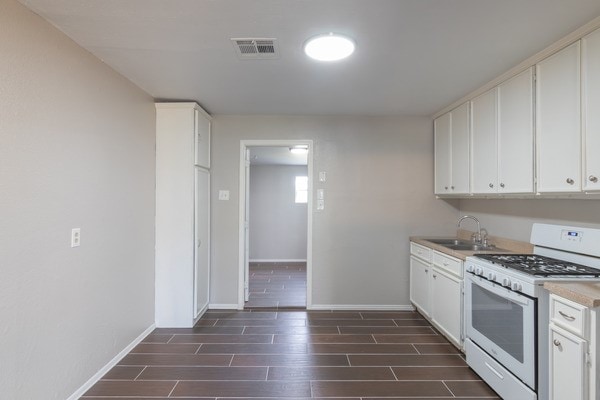 3322 Mccrarey Dr, Houston, TX 77088 - kitchen featuring white gas range, wood finish floors, a sink, baseboards, and white cabinetry