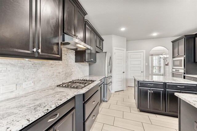 14907 Somerset Horizon Ln, Houston, TX 77044 - kitchen with stainless steel appliances, under cabinet range hood, decorative backsplash, arched walkways, and light stone countertops