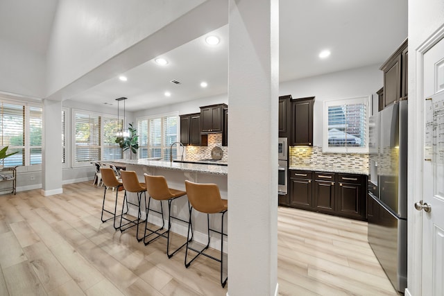 8442 Horsepen Bend Dr, Conroe, TX 77385 - kitchen with stainless steel appliances, a kitchen bar, decorative backsplash, dark brown cabinets, and light stone counters