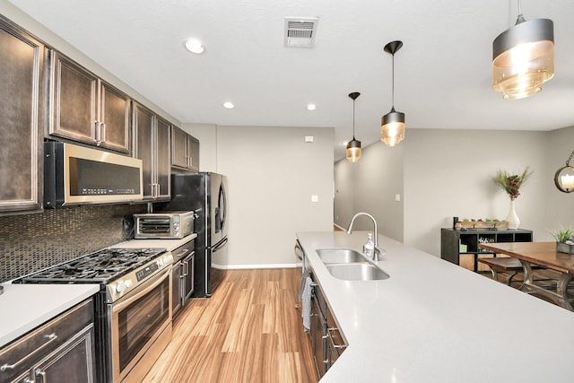 22619 Bellwick Ridge Ln, Katy, TX 77449 - kitchen featuring appliances with stainless steel finishes, a sink, light wood-style floors, dark brown cabinets, and pendant lighting