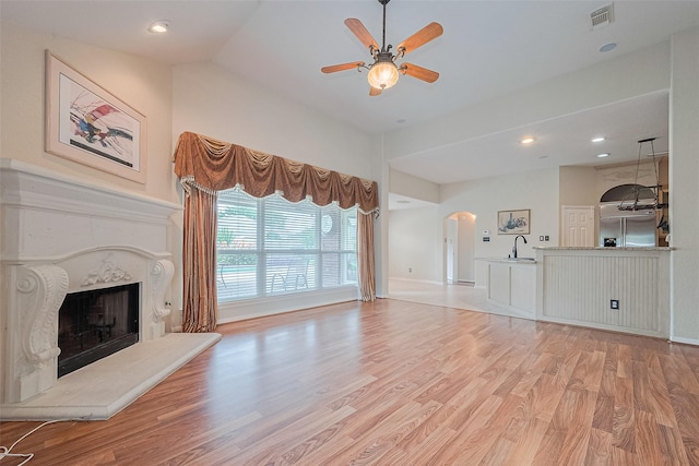 14202 Valley Bend Ct, Sugar Land, TX 77498 - unfurnished living room featuring arched walkways, a sink, light wood-type flooring, a premium fireplace, and ceiling fan