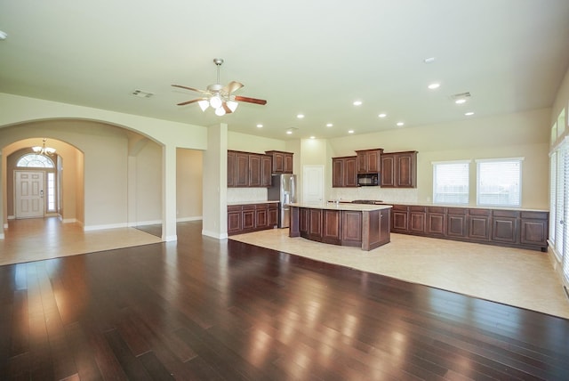 14110 Green Thicket Dr, Pearland, TX 77584 - kitchen with black microwave, arched walkways, open floor plan, a kitchen island with sink, and light countertops