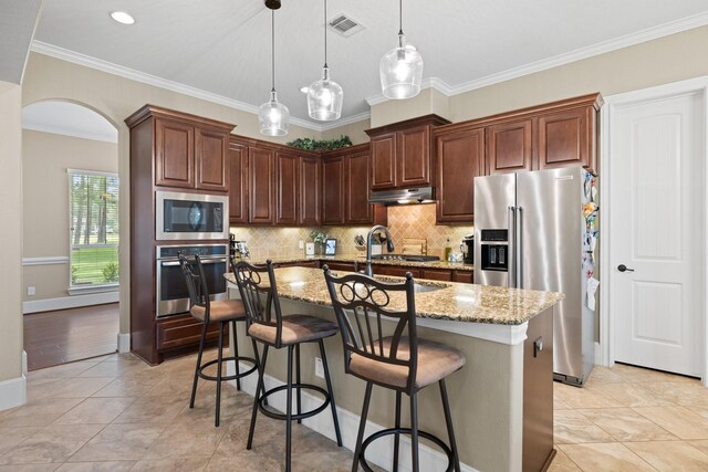 29122 Champions Dr, Magnolia, TX 77355 - kitchen with stainless steel appliances, under cabinet range hood, light stone countertops, backsplash, and arched walkways