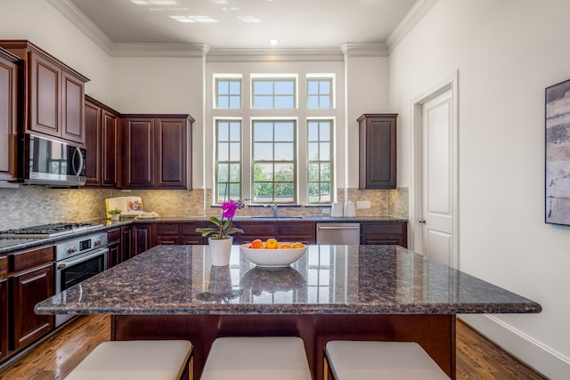 1217 E 28th St, Houston, TX 77009 - kitchen featuring stainless steel appliances, a kitchen breakfast bar, dark wood finished floors, crown molding, and tasteful backsplash