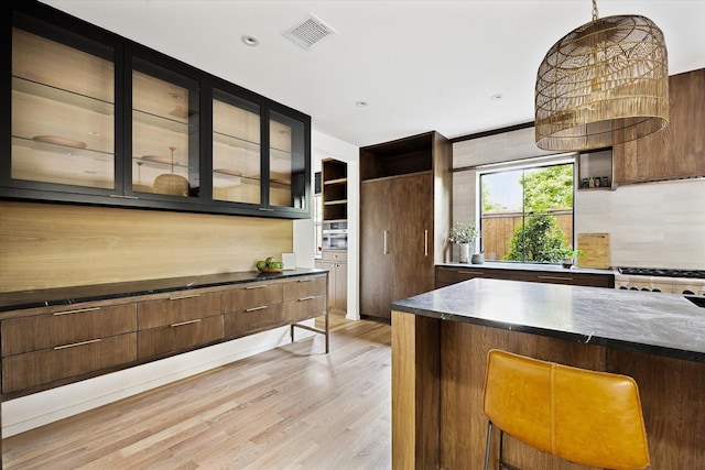 703 E 9th St, Houston, TX 77007 - kitchen with light wood-type flooring, glass insert cabinets, decorative backsplash, a kitchen bar, and stove