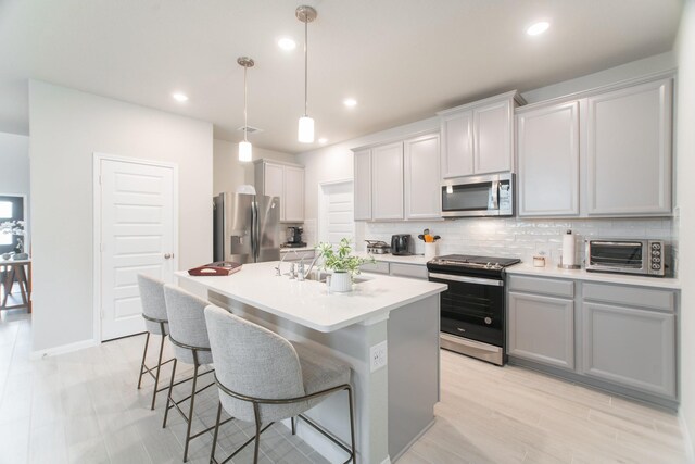 17542 Rosette Grass Dr, Conroe, TX 77385 - kitchen with stainless steel appliances, decorative backsplash, a kitchen island with sink, a breakfast bar area, and recessed lighting