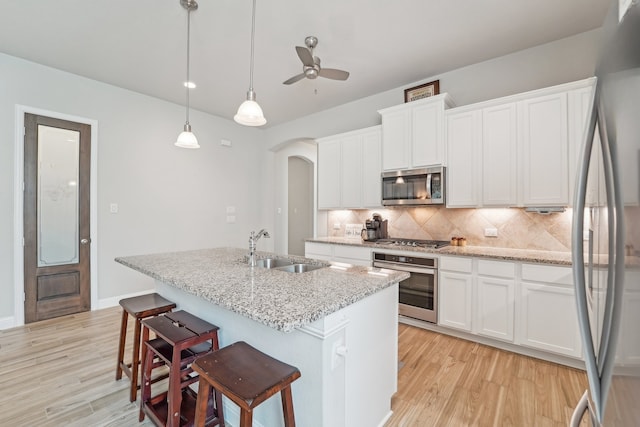 10029 Red Beadtree Pl, Conroe, TX 77385 - kitchen featuring appliances with stainless steel finishes, a sink, arched walkways, tasteful backsplash, and light wood-type flooring