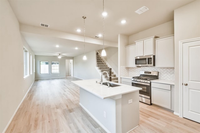 19253 Hazel Firs Ct, Magnolia, TX 77355 - kitchen with appliances with stainless steel finishes, a sink, light wood-style flooring, backsplash, and a center island with sink