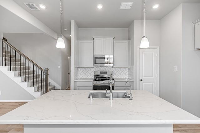 19253 Hazel Firs Ct, Magnolia, TX 77355 - kitchen featuring appliances with stainless steel finishes, a sink, light wood-type flooring, a kitchen island with sink, and tasteful backsplash